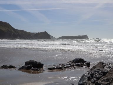 A rocky beach with waves and cliffs in the background at Berts Barn in Mullion