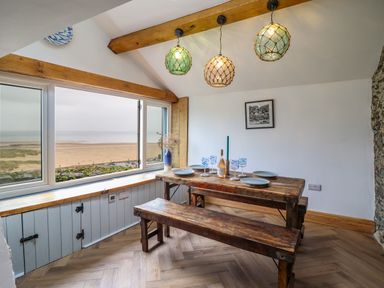 A dining room with a wooden table and benches overlooking a beach at Pengarreg in Barmouth