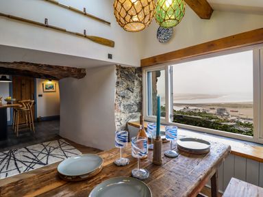 A dining area with a wooden table set with plates and glasses next to a window overlooking a coastal view at Pengarreg in Barmouth