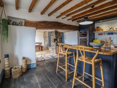 A kitchen with wooden beams blue island and bar stools next to a dining area with stone wall at Pengarreg in Barmouth