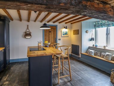 A kitchen with wooden beams a wooden island with two stools a window seat with cushions and a wooden door at Pengarreg in Barmouth