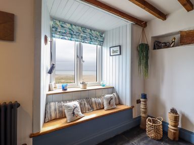 A window seat with cushions and small decor items in a room with wooden beams and a hanging plant at Pengarreg in Barmouth