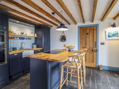 A kitchen with wooden beams on the ceiling and a wooden island with stools at Pengarreg in Barmouth