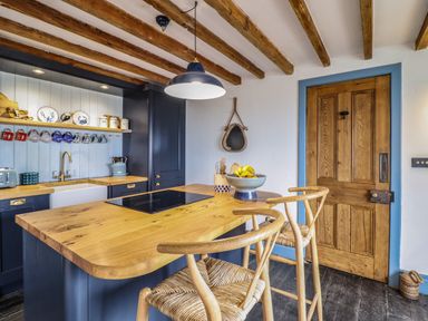 A kitchen with wooden beams on the ceiling a wooden door with blue trim a wooden island with two chairs and a bowl of fruit at Pengarreg in Barmouth
