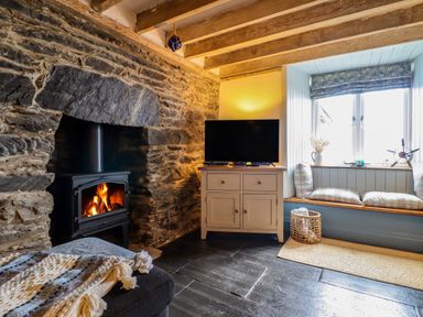 A living room with a stone fireplace with a wood stove a cabinet with a television and a window seat at Pengarreg in Barmouth