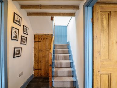 A stairway with blue painted sides and a carpet runner next to a wooden door and framed pictures on the wall at Pengarreg in Barmouth