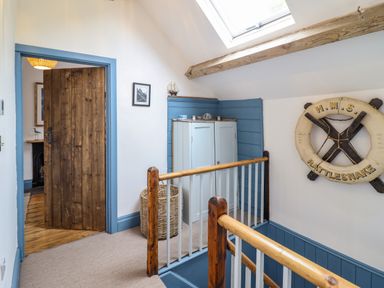A hallway with wooden bannisters a closed wooden door a cupboard a woven basket and a life buoy on the wall at Pengarreg in Barmouth