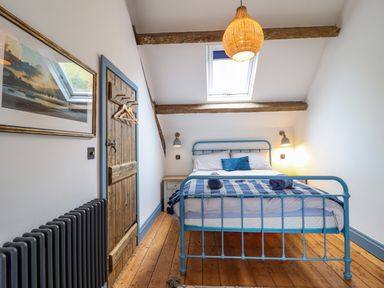 A bedroom with a blue metal bed frame wooden floor and ceiling beams at Pengarreg in Barmouth
