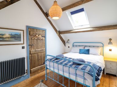 A bedroom with a blue metal bed frame, wooden floor, skylight, and a wooden door at Pengarreg in Barmouth