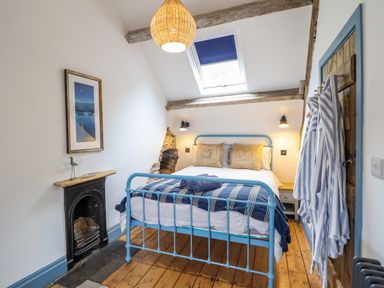 A bedroom with a blue metal bed frame, wooden floor, skylight window, striped robes hanging on a wooden door and a small fireplace at Pengarreg in Barmouth