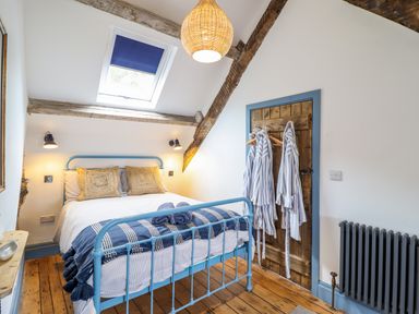 A bedroom with a blue metal bed frame wooden floor skylight and robes hanging on a wooden door at Pengarreg in Barmouth