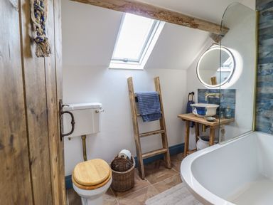 A bathroom with a toilet wooden seat wooden ladder with towel wooden sink stand round mirror and bathtub at Pengarreg in Barmouth