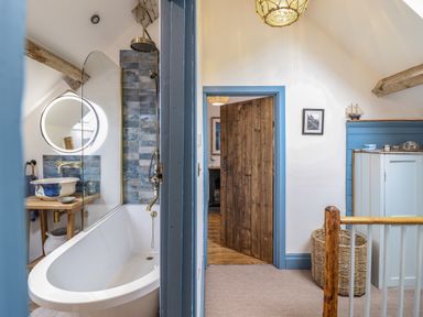 A bathroom with a bathtub and a sink next to a hallway with a door and a wicker basket at Pengarreg in Barmouth