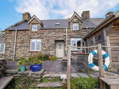 Stone house with gray door and windows flower pots and wooden deck with life buoy at Pengarreg in Barmouth