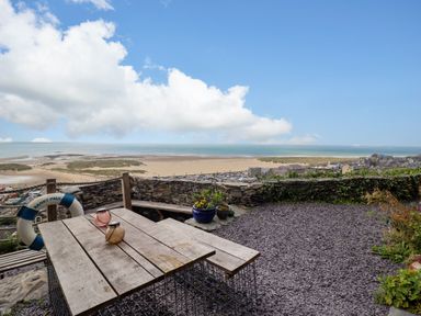 An outdoor seating area with a wooden table and bench overlooking a beach and ocean at Pengarreg in Barmouth