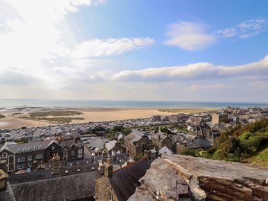A coastal town with rooftops overlooking a beach parking area and the sea at Pengarreg in Barmouth