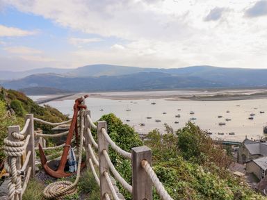 A view of a river with boats and hills in the background from a hill with rope fence and an anchor in Pengarreg in Barmouth