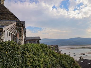 A stone and wooden house with green ivy overlooking a bay with boats and hills in the background at Pengarreg in Barmouth
