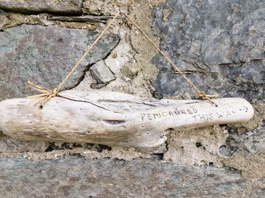 A wooden sign with the text pencarreg this way hanging on a stone wall at Pengarreg in Barmouth