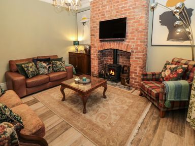 A living room with a wood stove in a brick fireplace a leather sofa a plaid armchair and a wooden coffee table at Sunflowers in Earsdon near Whitley Bay