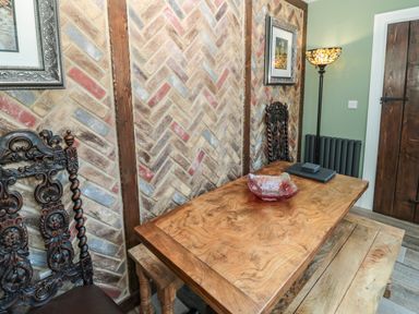 A dining area with a wooden table, carved wooden chairs, a bench, a floor lamp, framed pictures on the wall at Sunflowers in Earsdon near Whitley Bay
