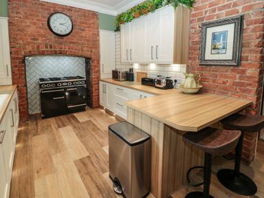 A kitchen with brick walls white cabinets wooden countertops a black stove and bar stools at Sunflowers in Earsdon near Whitley Bay
