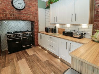 A kitchen with white cabinets wooden countertops a black oven and a clock on a red brick wall at Sunflowers in Earsdon near Whitley Bay