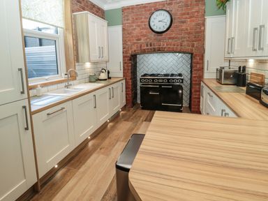 A kitchen with white cabinets wooden countertops a black stove brick wall and clock at Sunflowers in Earsdon near Whitley Bay