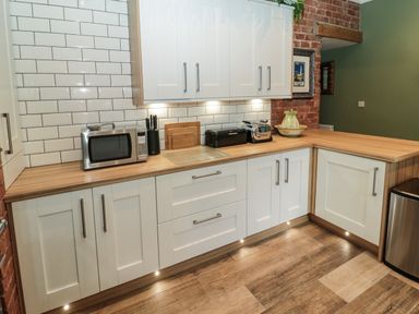 A kitchen with white cabinets a wooden countertop a microwave knife block toaster bread box and a green ceramic vase at Sunflowers in Earsdon near Whitley Bay