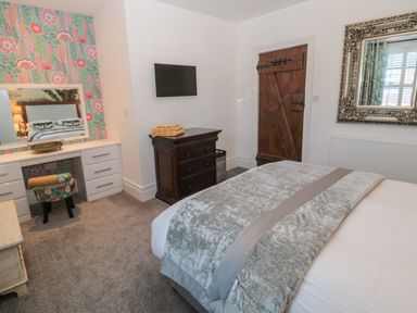 A bedroom with a bed a wooden chest of drawers a wall-mounted TV a dressing table with a chair and a large mirror at Sunflowers Earsdon near Whitley Bay