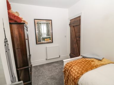 A small bedroom with a wooden wardrobe a mirror on the wall a bed with a mustard blanket and a wooden door at Sunflowers Earsdon near Whitley Bay
