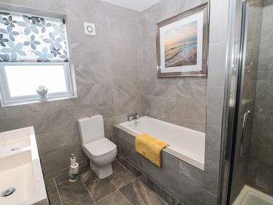 A bathroom with a bathtub a toilet a window with floral shade a double sink and a glass shower enclosure at Sunflowers in Earsdon near Whitley Bay