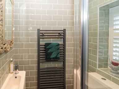 A bathroom with green tiled walls a towel rack with a towel a sink with soap and a mirror at Sunflowers in Earsdon near Whitley Bay
