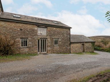 A stone barn with two windows and a double glass door surrounded by gravel and grass at Brimpts Barn Dartmeet near Princetown