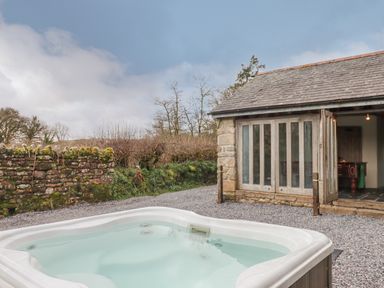 An outdoor hot tub next to a stone building with folding glass doors and a gravel ground at Brimpts Barn in Dartmeet near Princetown