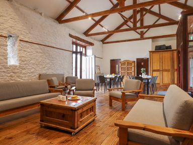 A sitting area with sofas and armchairs around a wooden coffee table and dining tables with chairs in a room with wooden beams and white stone walls at Brimpts Barn Dartmeet near Princetown