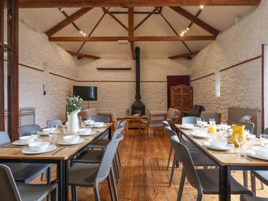 A dining room with wooden floor tables set with plates and glasses a television and seating area with armchairs and a wood stove at Brimpts Barn Dartmeet near Princetown
