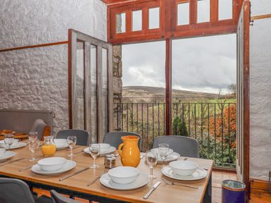 A dining room with a table set for six near open wooden doors showing a view of hills and greenery at Brimpts Barn in Dartmeet near Princetown