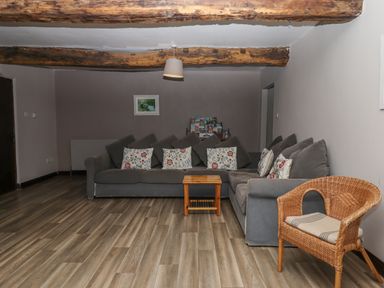 A living room with a gray sectional sofa with floral pillows a wooden side table and a wicker chair at Brimpts Barn Dartmeet near Princetown