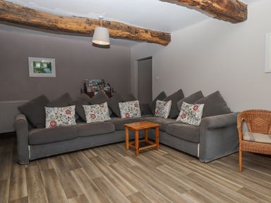 A living room with a grey sectional sofa with floral cushions a wooden coffee table and a wicker chair at Brimpts Barn Dartmeet near Princetown