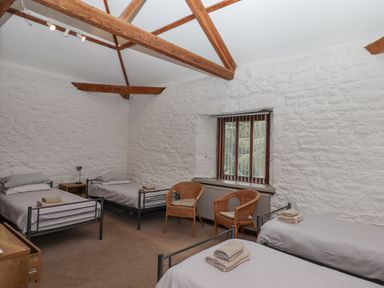 A bedroom with four single metal frame beds two wicker chairs and a wooden window at Brimpts Barn Dartmeet near Princetown