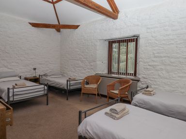 A bedroom with four single beds wooden beams on the ceiling a window two wicker chairs and a side table at Brimpts Barn Dartmeet near Princetown