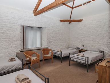 A bedroom with four single beds two wicker chairs a wooden nightstand and exposed wooden beams at Brimpts Barn Dartmeet near Princetown