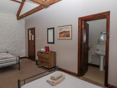 A bedroom with two single beds a wooden dresser with a kettle cups a mirror a framed picture and a bathroom doorway at Brimpts Barn in Dartmeet near Princetown