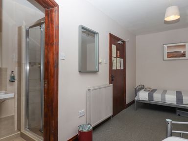 A small bedroom with a single bed a wall-mounted mirror a radiator a door with notices and an en suite shower at Brimpts Barn Dartmeet near Princetown