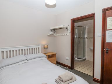 A bedroom with a double bed white headboard side table and lamp with an open door to a tiled bathroom at Brimpts Barn Dartmeet near Princetown