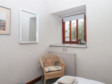 A small room corner with a wicker chair, a window, a mirror on the wall, and a kettle on the windowsill at Brimpts Barn Dartmeet near Princetown