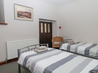 A bedroom with two single beds with striped bedding a wicker chair and a framed landscape picture on the wall at Brimpts Barn Dartmeet near Princetown