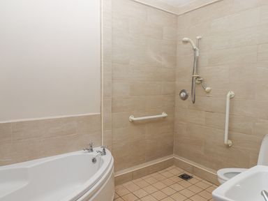 A bathroom with a corner bathtub a wall-mounted shower a toilet and grab bars at Brimpts Barn in Dartmeet near Princetown