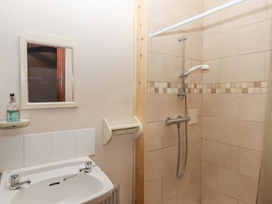 A bathroom with a sink, mirror, soap dispenser, and a tiled shower at Brimpts Barn in Dartmeet near Princetown